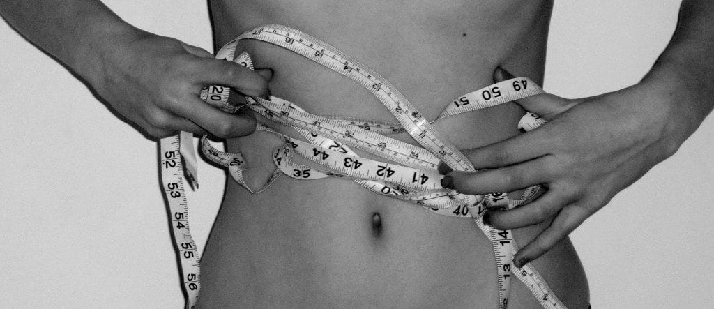 medidas - mulher atrapalhada para medir abdomen com fita metrica